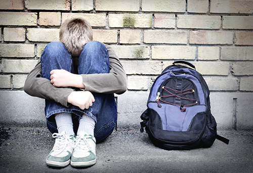 boy holding his knees against the wall with his backpack next to him