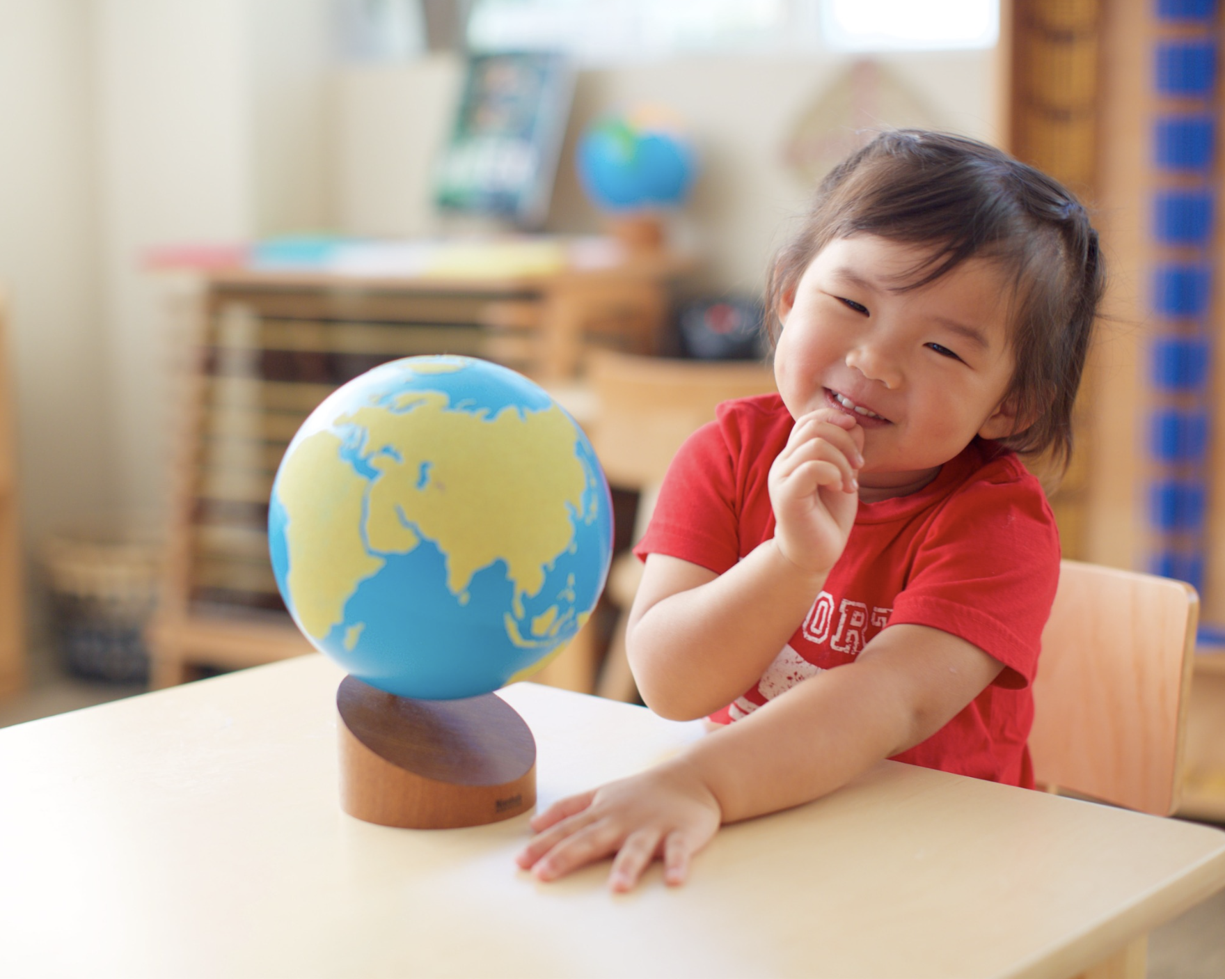 A little girl smiling next to a globe of the world at LePort Montessori Best Montessori School
